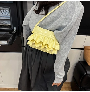 Detail of light yellow patent leather crossbody bag with tiered ruffle design and strap