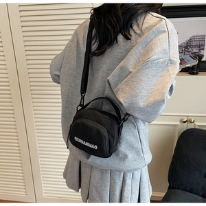 Detail of black canvas crossbody bag with white embroidery shown on female model