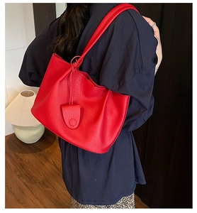 Detail view of large red pebble leather tote bag featuring a decorative round side charm