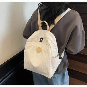 Detail of cream canvas backpack showing brown leather patch and durable black zippers