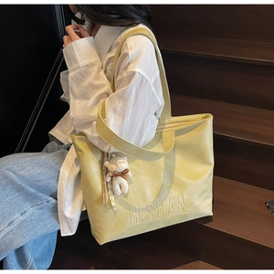 Close-up of bright yellow textured leather tote bag with H.SHAN embossed logo and bear charm