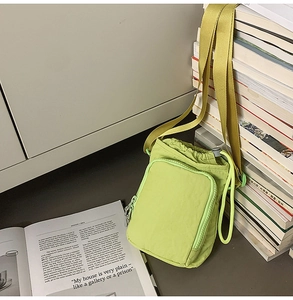 Detail of neon green nylon crossbody bag showing the drawstring closure and zipper pocket