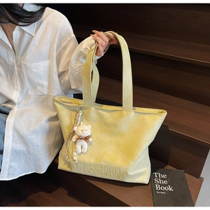 Detail of light green leather tote bag with H.SHAN logo and white plush bear charm