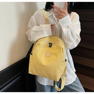 Detailed mirror selfie of a bright yellow canvas backpack with front zipper and logo patch