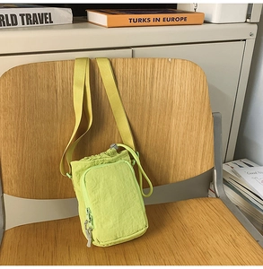 Detail of neon green nylon crossbody bag with drawstring closure and front zipper pocket