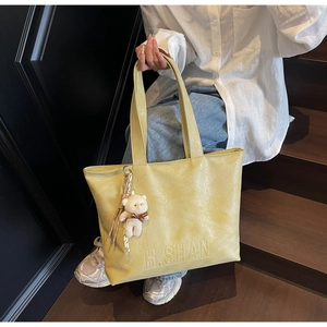 Detail of bright yellow leather tote bag featuring a textured finish and white bear charm