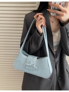 Chic light blue ruched underarm bag with bow detail shown on shoulder in indoor lighting