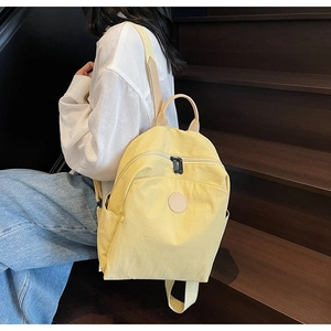Detailed side view of a light yellow nylon backpack on a model sitting on wooden steps