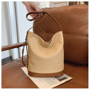 Detail of straw woven bucket bag with brown leather handles on a vintage sofa