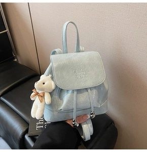 Detail of light blue pleated patent leather backpack with mini bear charm and relief text