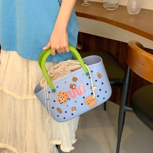 Detail of blue beach bag featuring green handles, charms, and a beige drawstring liner