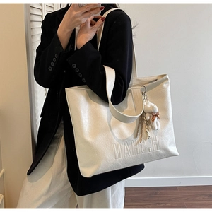 Detail of cream leather tote bag featuring embossed logo and fuzzy bear charm