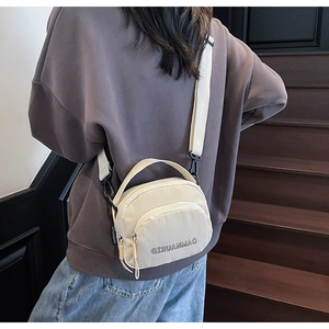 Detailed view of cream canvas crossbody bag featuring adjustable strap and front zipper