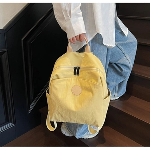 Handheld yellow nylon backpack featuring leather handle and round logo patch detail