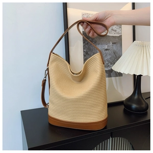 Close-up of woven bucket bag featuring brown leather base and reinforced stitching details