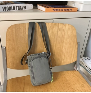 Gray-green nylon crossbody phone bag with drawstring closure hanging on a chair