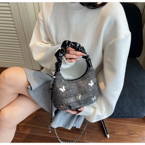 Detail of dark grey tweed dumpling bag featuring metallic butterfly charms and a chain
