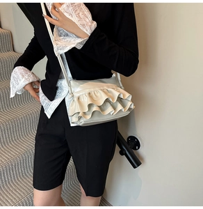 Model wearing a light beige pleated faux leather bucket bag with glossy finish details