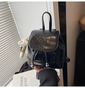 Detail of glossy black patent leather backpack with drawstring and plush bear charm