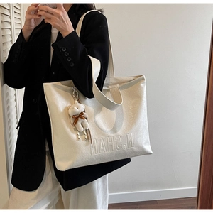 Close-up of cream tote bag featuring litchi grain texture and cute plush bear charm