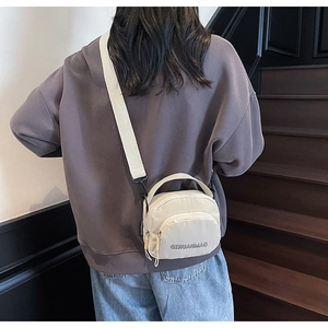 Rear view of a model wearing a light beige canvas crossbody bag on a wooden staircase