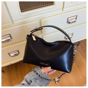 Detail of black crescent shoulder bag featuring silver metal chain and spherical charm