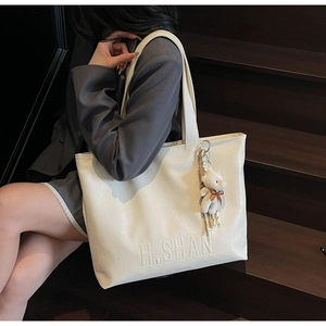 Detail of cream white tote bag with faux crocodile texture and a cute plush bear charm