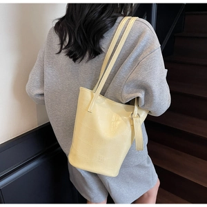 Detail of yellow crocodile embossed bucket bag featuring elegant branding on textured leather
