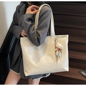 Detail of cream tote bag with H.SHAN embossed logo and cute plush bear accessory
