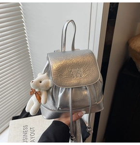 Detail of silver metallic bucket backpack with crushed texture and plush bear charm