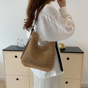 Detail of woven straw tote bag featuring mesh texture and dark brown leather shoulder strap