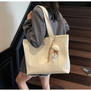Detail of minimalist cream tote bag with fine litchi grain and cute teddy bear pendant