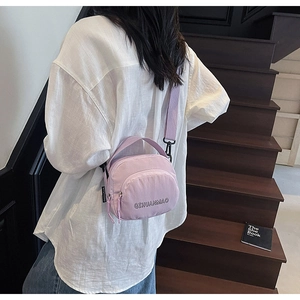 Detail of light purple canvas crossbody bag with adjustable strap and brand logo