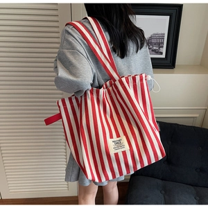 Detail of red and white striped canvas tote bag showing wide straps and drawstring closure
