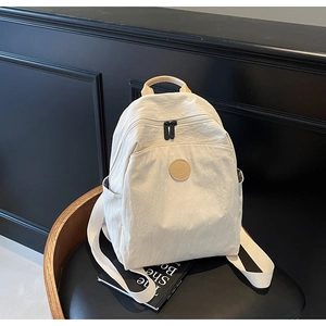 Detail of cream backpack showing dual zippers, side pockets, and adjustable nylon straps