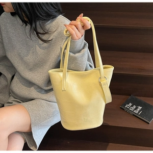Close-up of yellow crocodile embossed texture and metal ring details on a soft leather tote