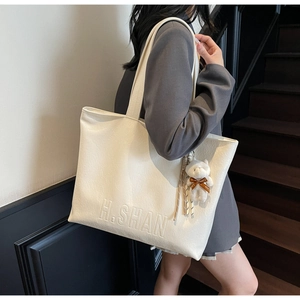 Detail shot of white textured leather tote bag with H.SHAN embossing and a bear charm