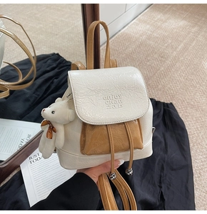 Detail of a beige pleated bucket backpack with a small plush bear and drawstring closure
