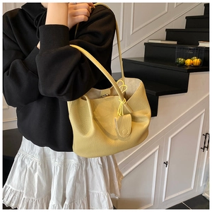 Detail of yellow lychee-textured tote bag with slender strap and metal buckle on model