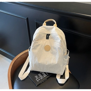 Close-up of a beige nylon backpack with brown leather accents on a black seat