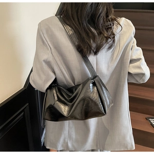 Detail einer schwarzen glänzenden Hobo-Tasche aus Kunstleder mit Faltenstruktur am Model