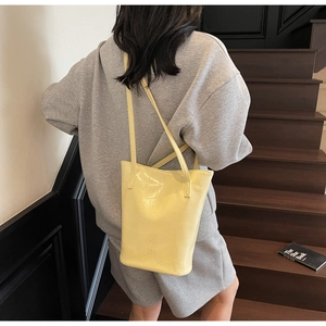 Detail of yellow bucket bag with crocodile texture and long shoulder straps on model