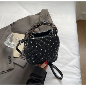 Detail of black quilted bucket bag featuring rhinestone studs and woven handle texture
