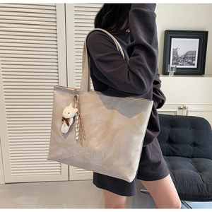 Detail of beige suede tote bag featuring H.SHAN logo and cute teddy bear pendant