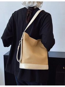 Minimalist woven straw bucket bag with white leather trim and adjustable shoulder strap