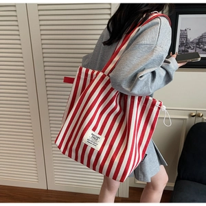Detail of red and white striped canvas tote bag with adjustable side drawstring and brand label