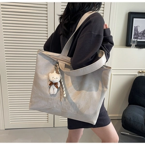 Detail of beige leather tote bag with embossed logo and cute white teddy bear pendant