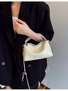 Minimalist beige crossbody bag with gold chain strap and metal logo on black blazer