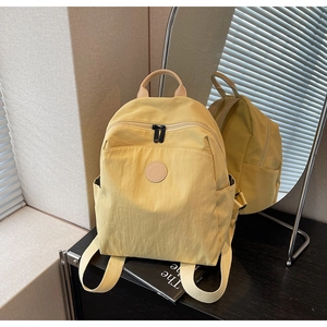 Detail of yellow nylon backpack with leather handle and side pockets in a mirror setup