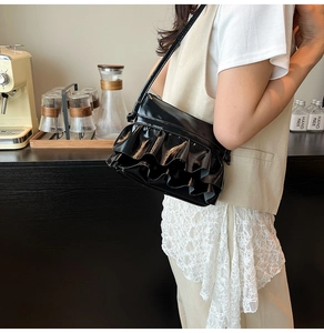 Detail of glossy black pleated ruffled leather handbag in a lifestyle cafe setting